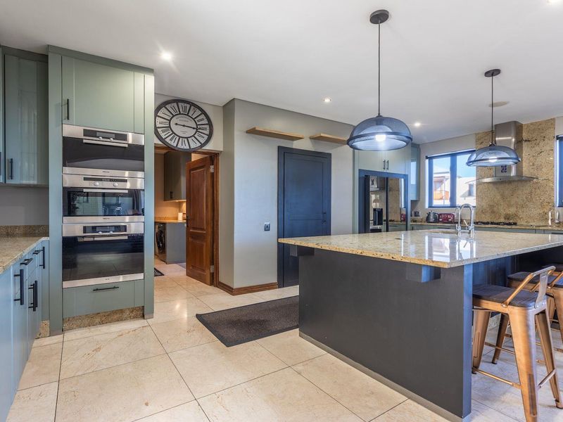 Modern kitchen featuring sage green cabinetry, granite countertops, a central island, built-in appliances, and tiled flooring with recessed and pendant lighting.