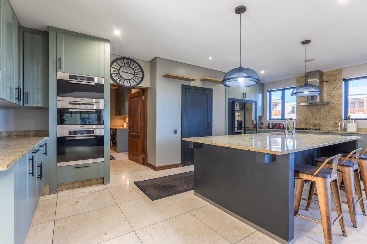 Modern kitchen featuring sage green cabinetry, granite countertops, a central island, built-in appliances, and tiled flooring with recessed and pendant lighting.