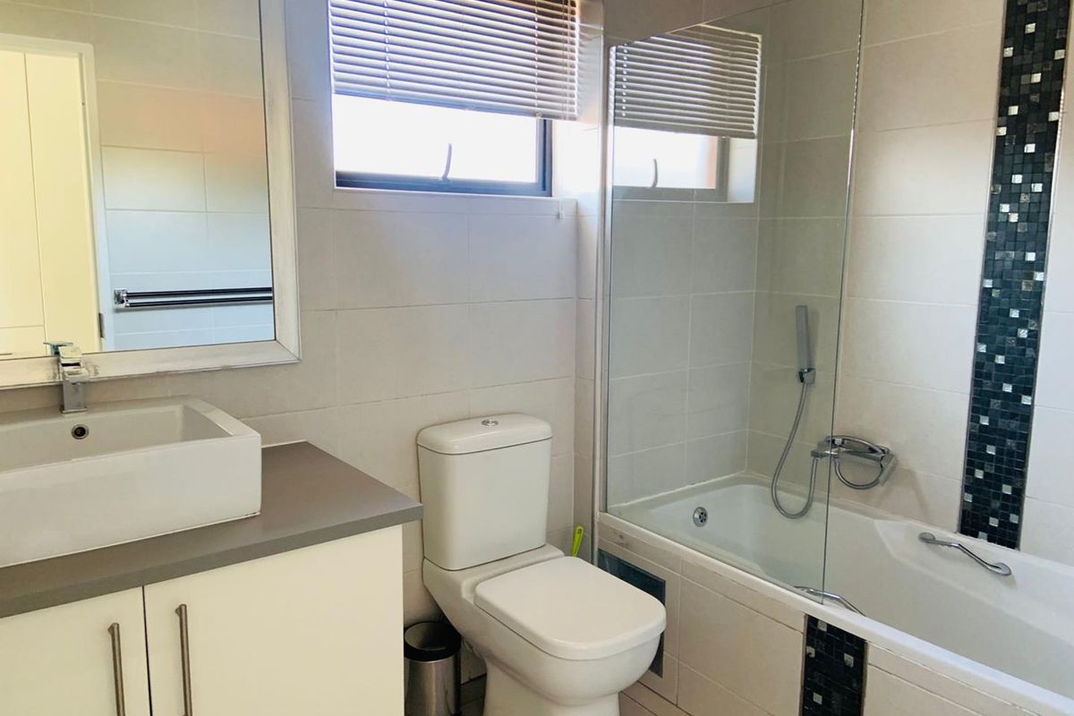 Modern bathroom featuring a vanity with a vessel sink, a toilet, and a bathtub with a glass shower screen and mosaic tile accents.