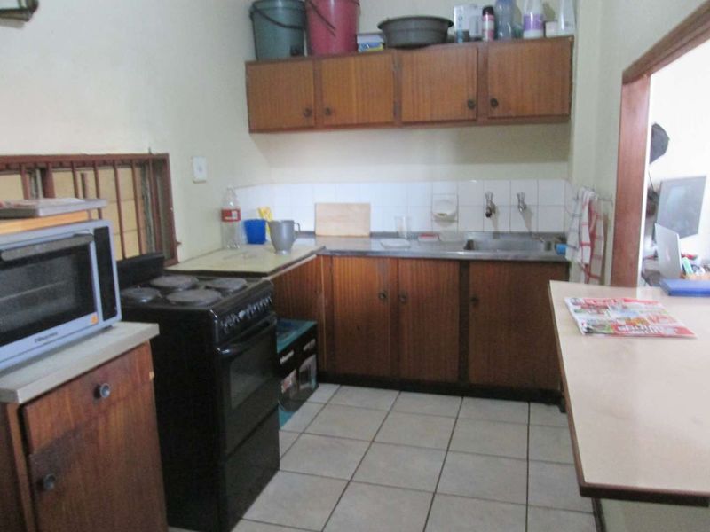 A dated kitchen featuring wooden cabinetry, tiled flooring, a stainless steel sink, and a tiled backsplash, offering potential for modernization.