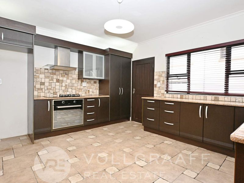 A spacious kitchen featuring dark wood cabinetry, granite countertops, a gas hob, built-in oven, and tiled flooring with a neutral backsplash.