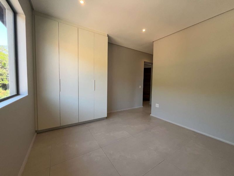 A bright, empty bedroom featuring neutral tiled flooring, built-in cupboards, and recessed downlighting, offering a clean and versatile space.