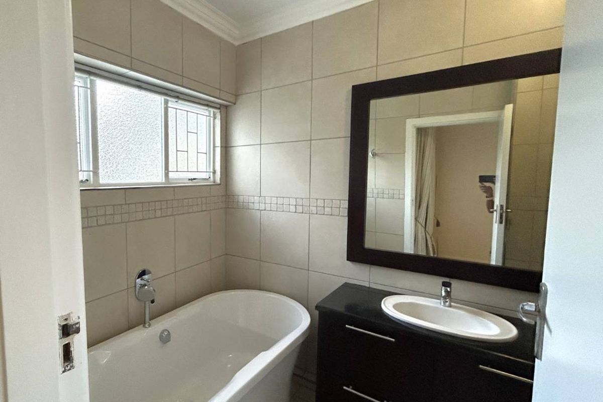 A clean, functional bathroom featuring a modern freestanding bathtub, a dark vanity cabinet with a basin, and neutral wall tiling.