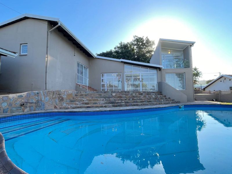 A spacious swimming pool area featuring stone-clad retaining walls, stone steps leading to the house, and secure access points to the main residence.