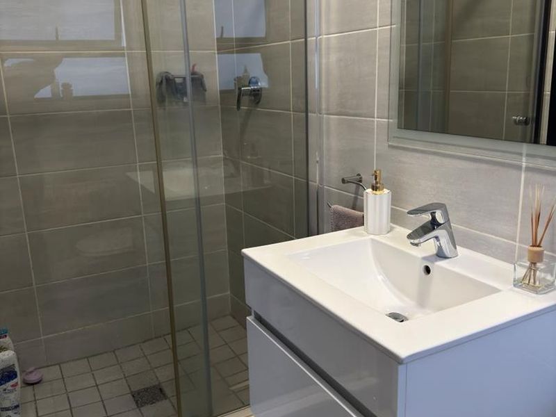Modern bathroom featuring a glass-enclosed shower, a sleek wall-mounted vanity with a ceramic basin, and neutral-toned wall and floor tiling.