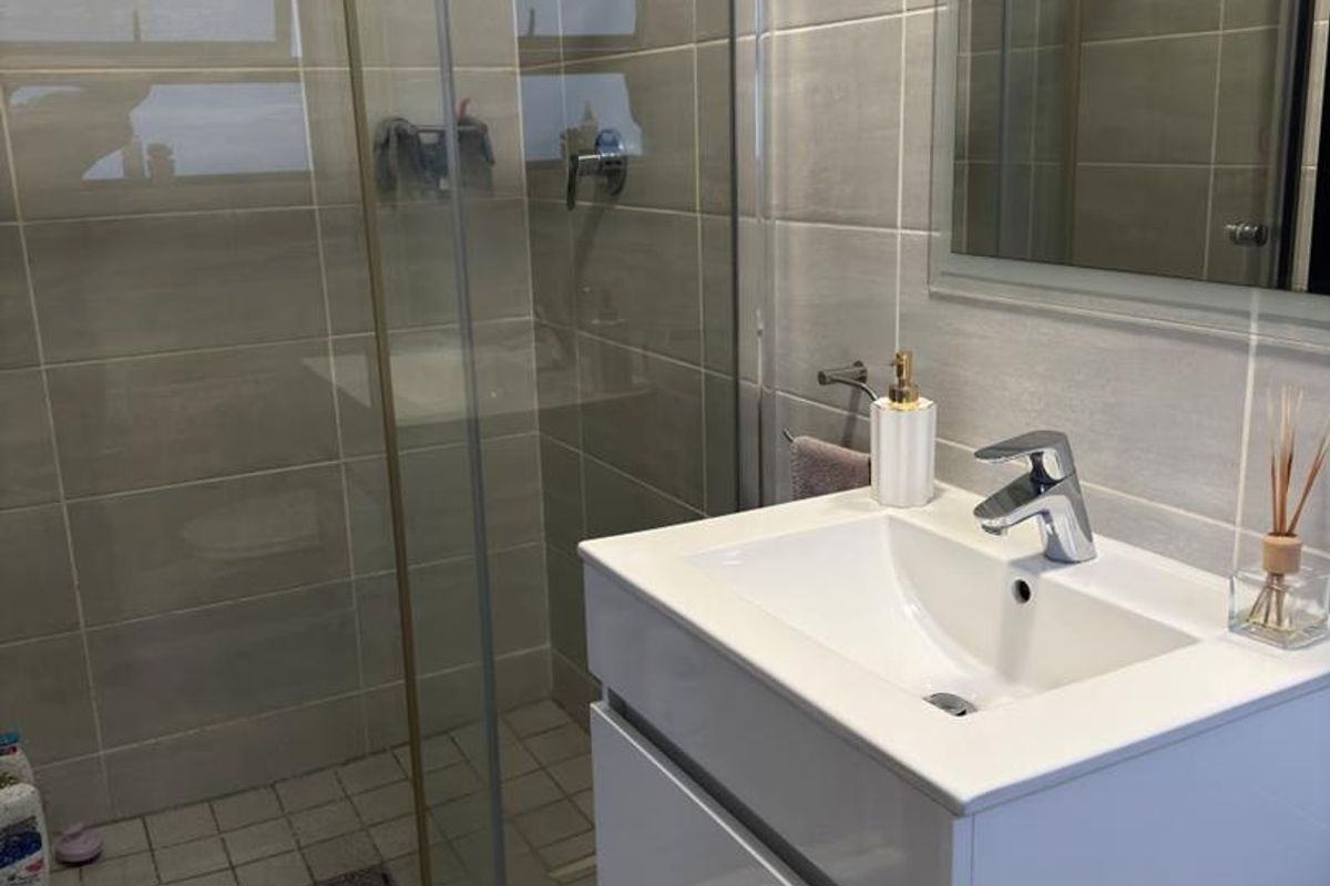 Modern bathroom featuring a glass-enclosed shower, a sleek wall-mounted vanity with a ceramic basin, and neutral-toned wall and floor tiling.