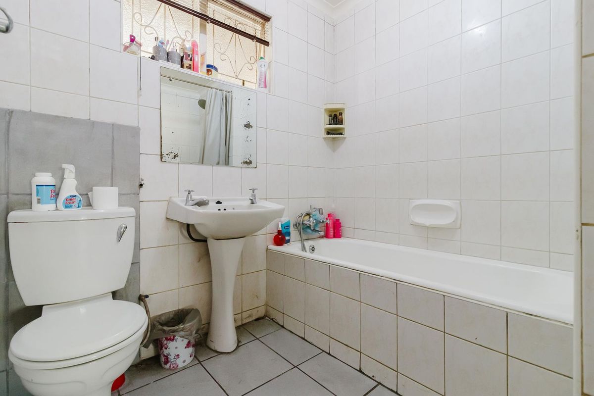 A functional bathroom featuring a pedestal basin, bathtub, and toilet with full-height wall tiling and a security-fitted window.