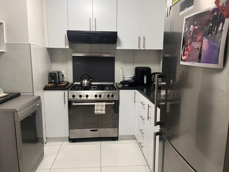 Compact kitchen featuring white cabinetry, granite countertops, tiled flooring, and a stainless steel gas stove with an integrated extractor fan.