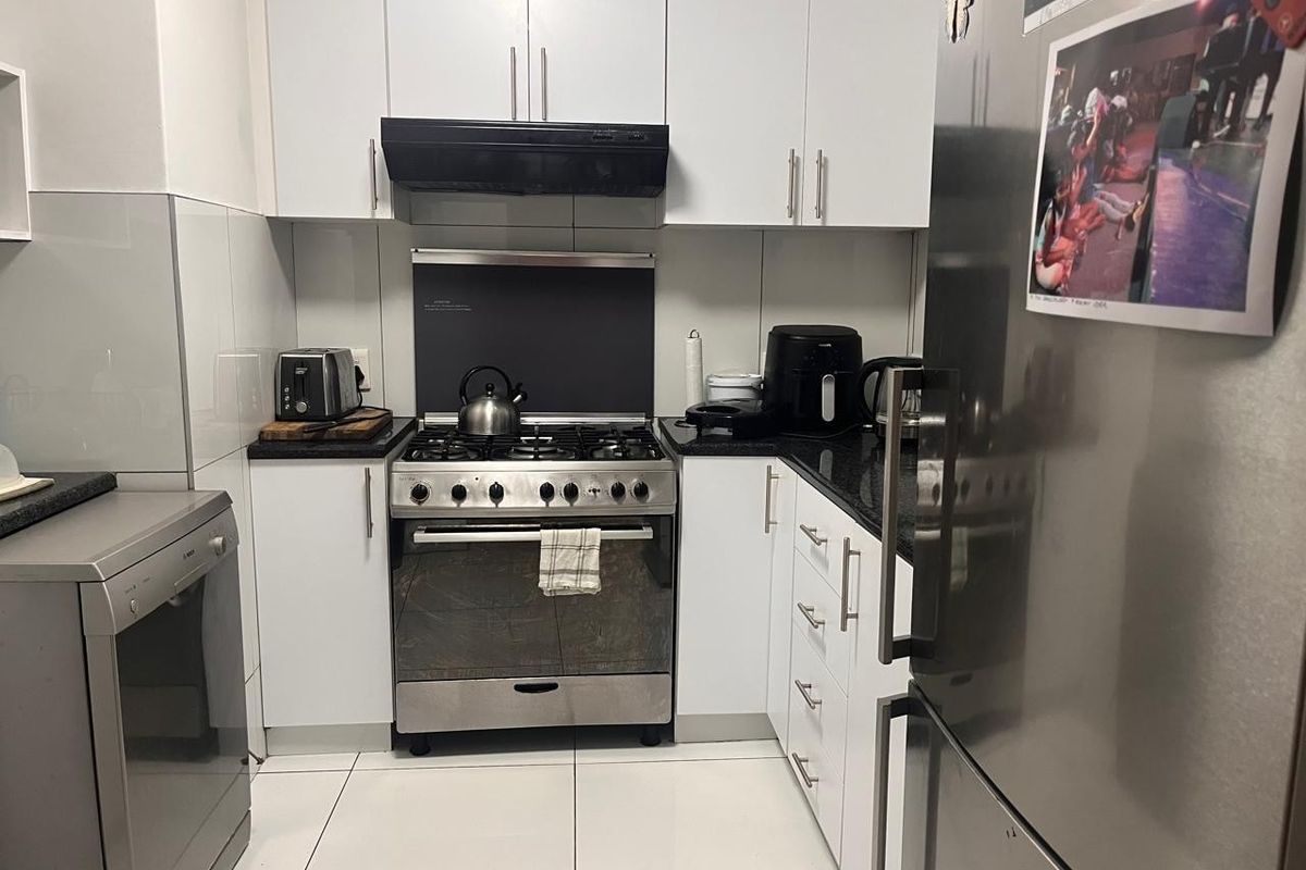 Compact kitchen featuring white cabinetry, granite countertops, tiled flooring, and a stainless steel gas stove with an integrated extractor fan.
