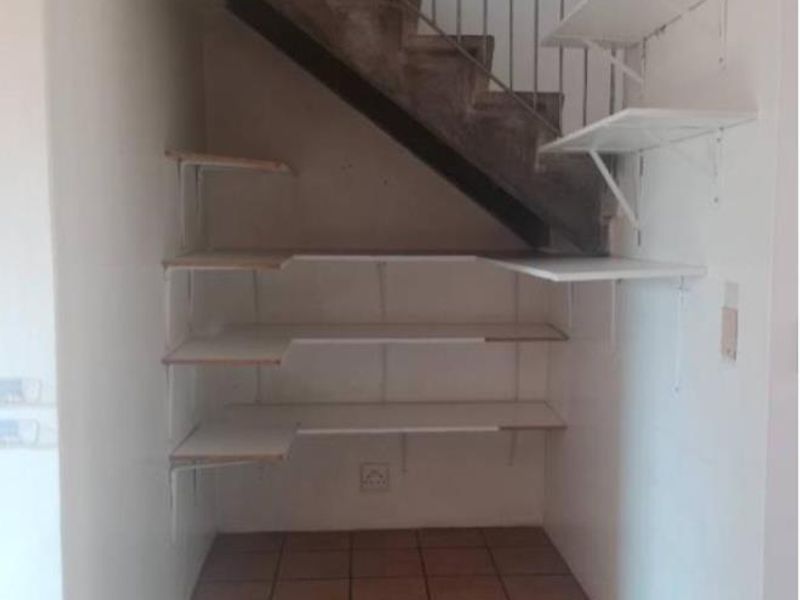 A utility space located under a staircase featuring tiled flooring and built-in wall shelving, offering potential for storage or a functional nook.