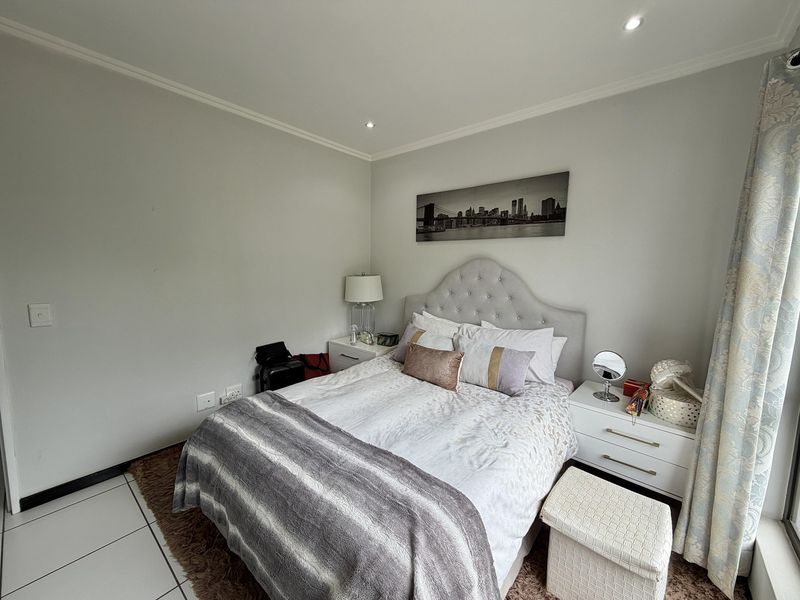 A well-maintained bedroom featuring neutral wall tones, recessed downlighting, and tiled flooring, providing a clean and comfortable living space.
