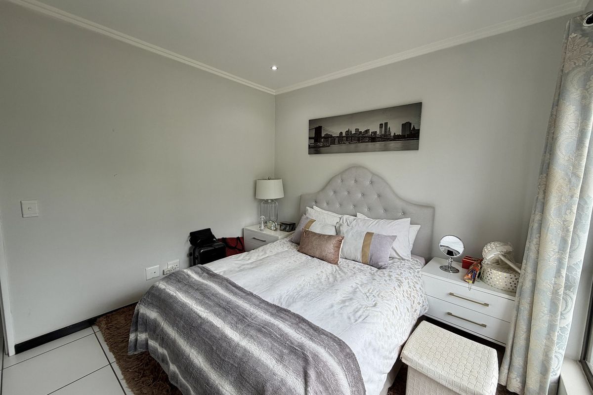 A well-maintained bedroom featuring neutral wall tones, recessed downlighting, and tiled flooring, providing a clean and comfortable living space.