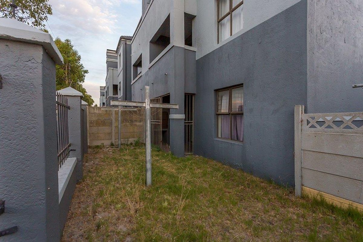 Rear exterior view of the apartment building featuring a small private garden area, perimeter walling, and security gates.