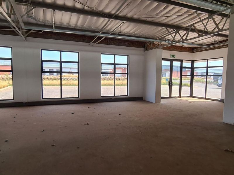 Spacious open-plan industrial unit featuring exposed steel roof trusses, concrete support columns, and large aluminium-framed windows providing ample natural light.