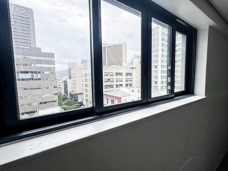An office space featuring large black aluminium-framed windows offering an expansive urban city view.