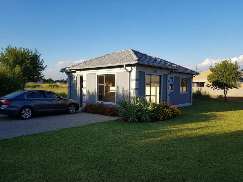 A well-maintained single-story residential building featuring a tiled roof, grey exterior finish, and a paved driveway set within a landscaped garden.