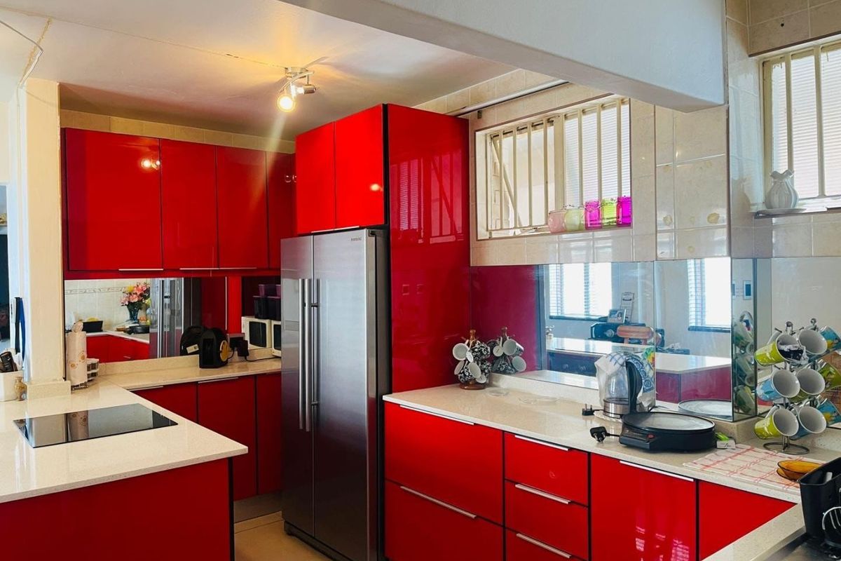 Modern kitchen featuring striking high-gloss red cabinetry, stone countertops, and a mirrored splashback, offering a bold and functional culinary space.