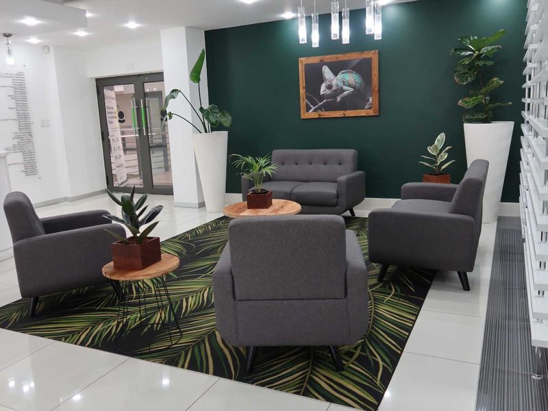 A modern, well-maintained office reception area featuring polished tiled floors, a bold green accent wall, and glass entrance doors.