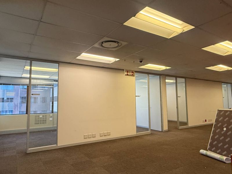 An open-plan office space featuring glass partitions, suspended ceilings with recessed lighting, and carpeted flooring, offering a versatile layout for professional use.