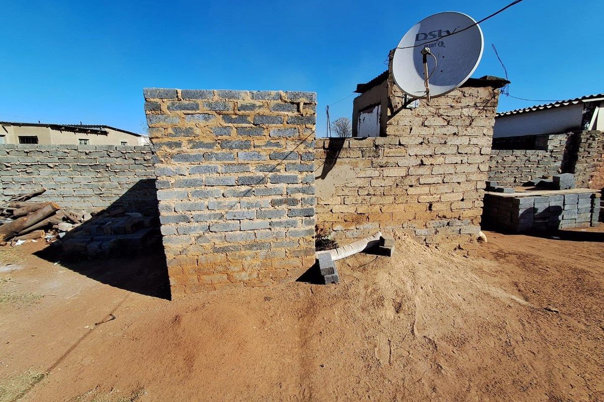 Rear exterior view of the property featuring unfinished brick structures, a boundary wall, and a satellite dish on a dirt lot.