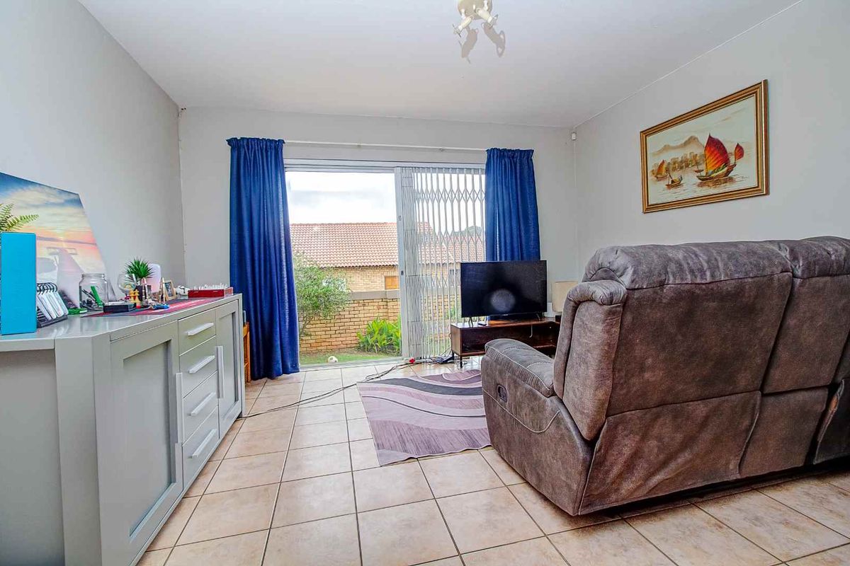 A living room featuring ceramic floor tiles and a sliding glass door with a security gate, providing direct access to the rear garden area.