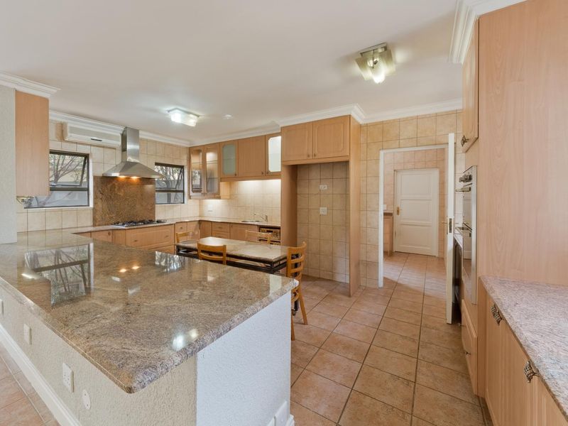 Spacious kitchen featuring granite countertops, built-in cabinetry, integrated oven, gas hob, and tiled finishes, with an adjacent scullery area.