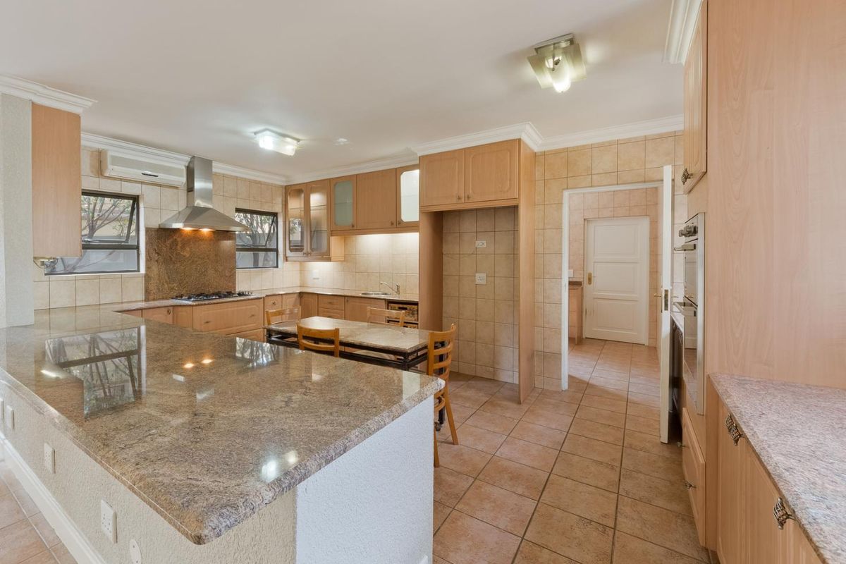 Spacious kitchen featuring granite countertops, built-in cabinetry, integrated oven, gas hob, and tiled finishes, with an adjacent scullery area.