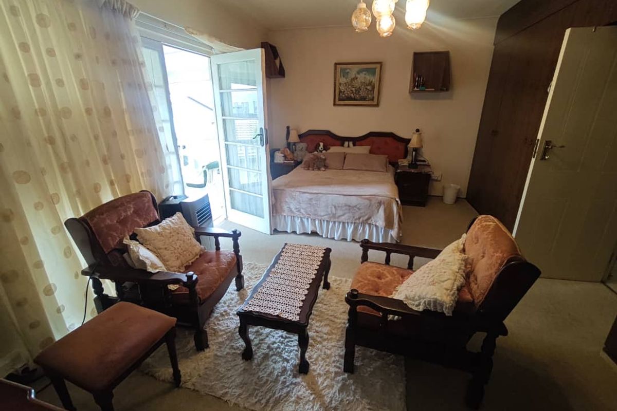 A spacious bedroom featuring built-in cupboards, carpeted flooring, and direct access to an outdoor area through a glass-paneled door.