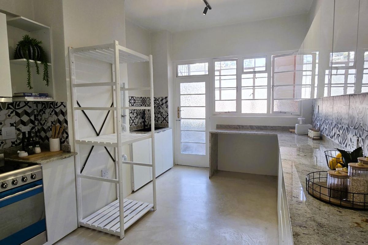 Modern kitchen featuring granite countertops, patterned tile backsplash, gas stove with extractor fan, and ample built-in cabinetry with direct access to the exterior.