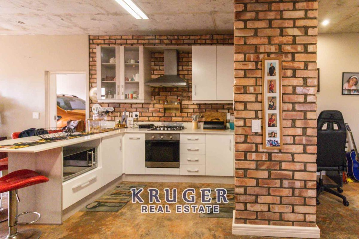 A kitchen featuring white cabinetry, a built-in oven and hob, extractor fan, and a distinctive exposed brick feature pillar.