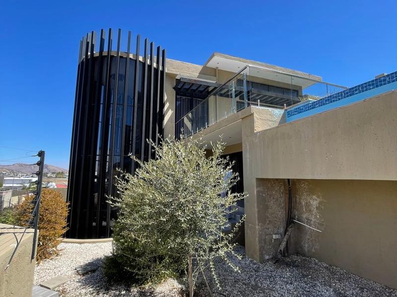 Rear exterior view of a modern home featuring a swimming pool, glass balustrades, and distinctive vertical architectural fins.