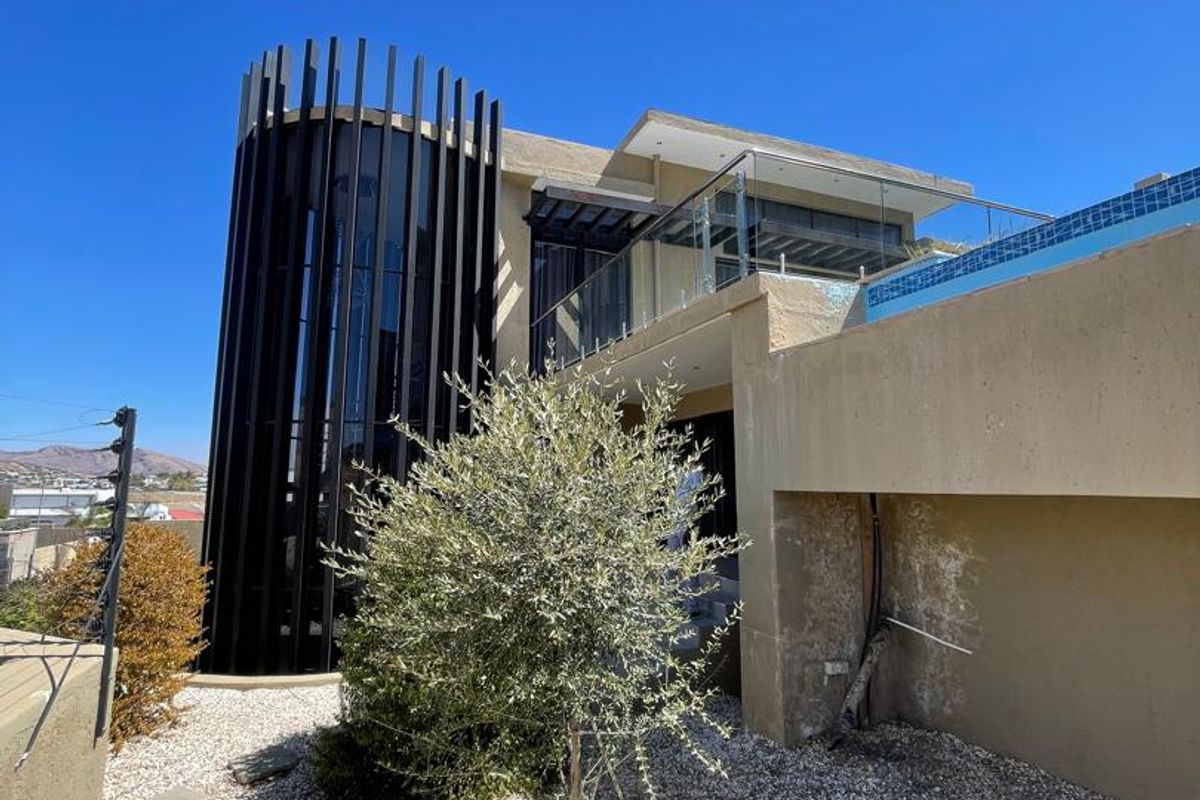 Rear exterior view of a modern home featuring a swimming pool, glass balustrades, and distinctive vertical architectural fins.