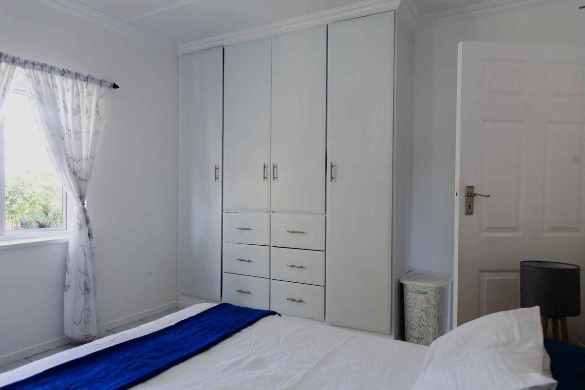 A bedroom featuring built-in white cabinetry with integrated drawers and hanging space, providing ample storage.
