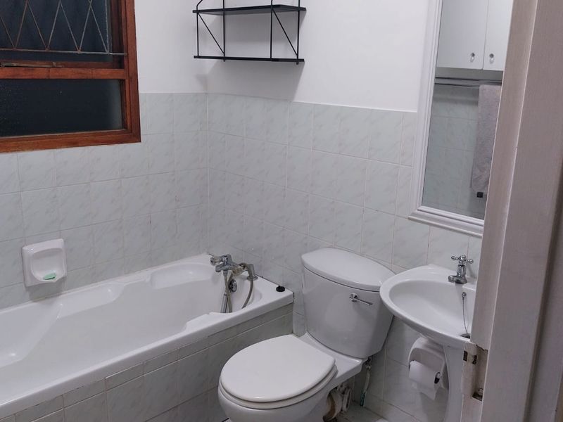 A functional bathroom featuring a standard bathtub, pedestal sink, toilet, and tiled wall finishes, offering a clean and practical layout.