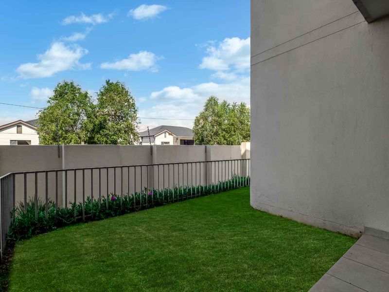 A private rear garden area featuring a well-maintained lawn, paved patio section, and secure perimeter walling with metal fencing.