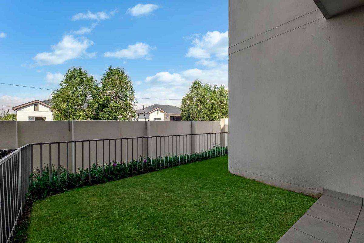 A private rear garden area featuring a well-maintained lawn, paved patio section, and secure perimeter walling with metal fencing.