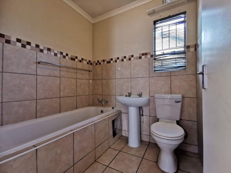 A functional bathroom featuring a bathtub, pedestal basin, and toilet with neutral tiled finishes and a window for natural light.