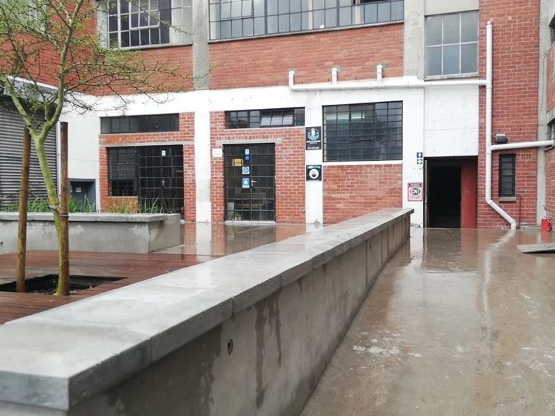 An industrial-style rear courtyard featuring exposed brickwork, steel-framed windows, a concrete retaining wall, and timber decking in a mixed-use property setting.