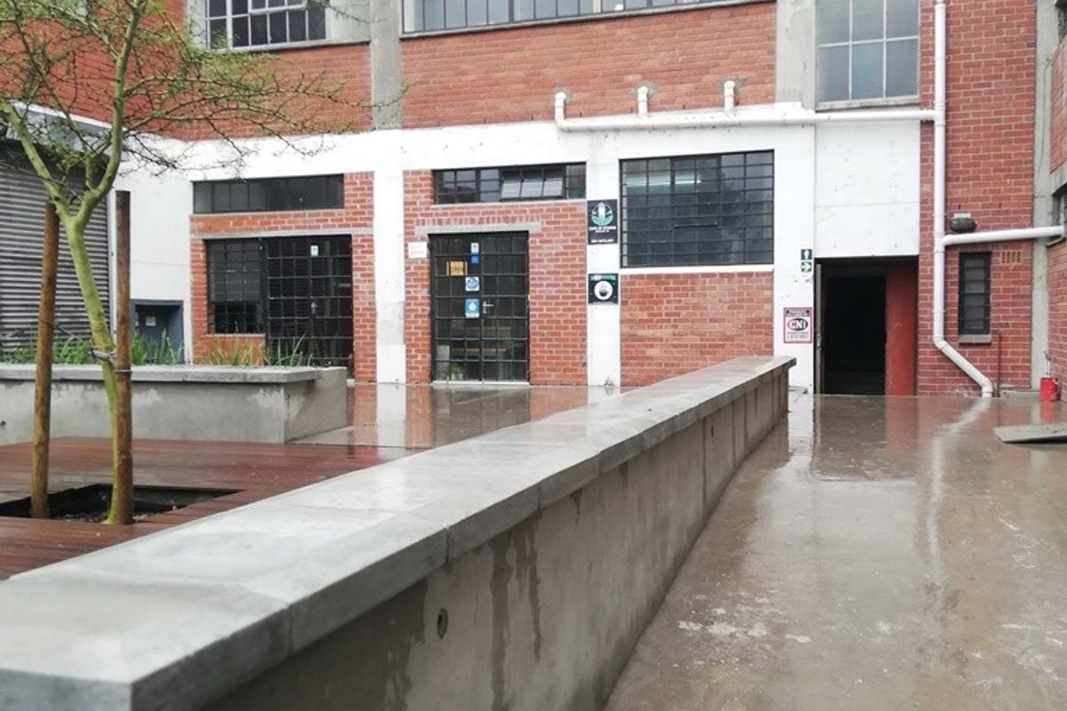 An industrial-style rear courtyard featuring exposed brickwork, steel-framed windows, a concrete retaining wall, and timber decking in a mixed-use property setting.
