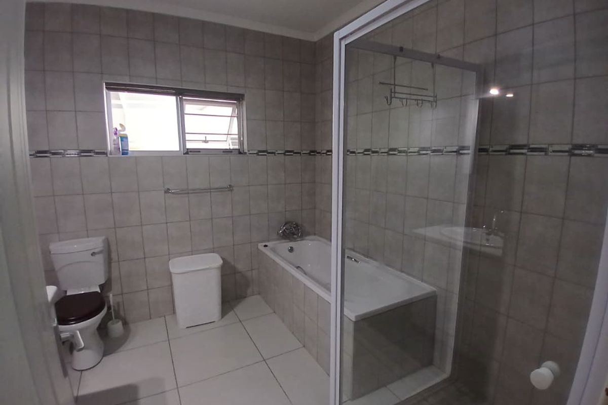 A functional bathroom featuring a built-in bathtub, a separate glass-enclosed shower, and neutral wall and floor tiling.