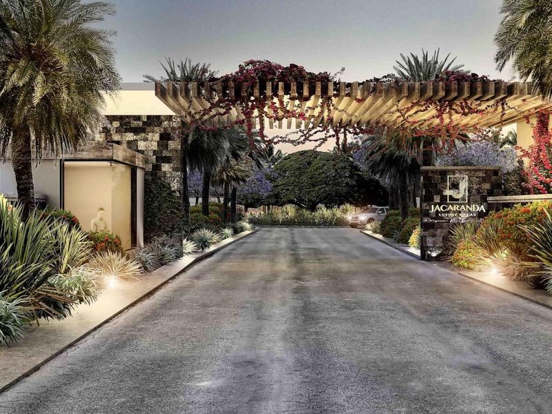 A grand, landscaped entrance to Jacaranda Luxury Villas, featuring a timber pergola, stone-clad signage, and manicured gardens.