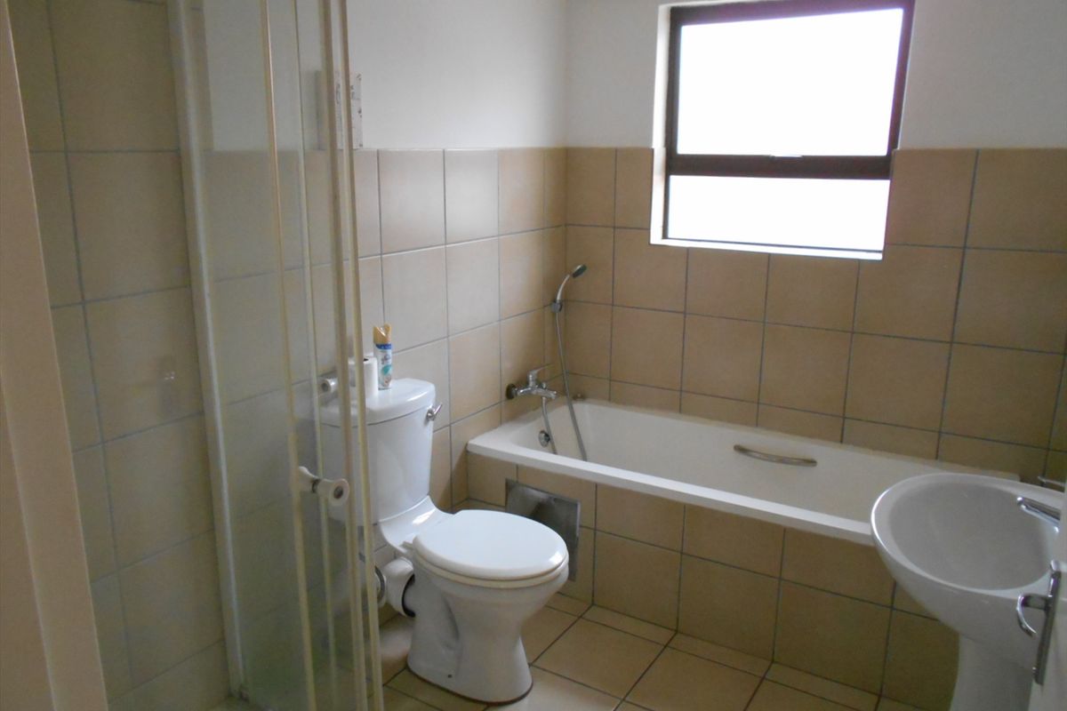 A functional bathroom featuring a combined shower and bathtub, pedestal basin, and toilet with neutral wall and floor tiling.
