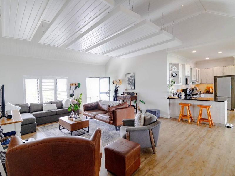 Spacious open-plan living area featuring a vaulted ceiling with decorative beams, laminate flooring, and a modern kitchen with a breakfast island and granite countertops.