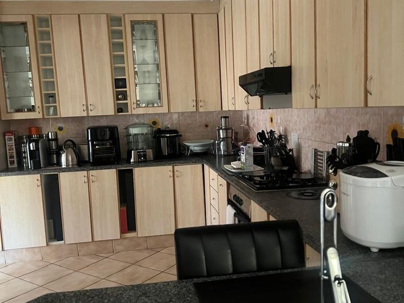 A functional kitchen featuring light wood-tone cabinetry, dark granite countertops, a gas hob with extractor fan, and tiled flooring.