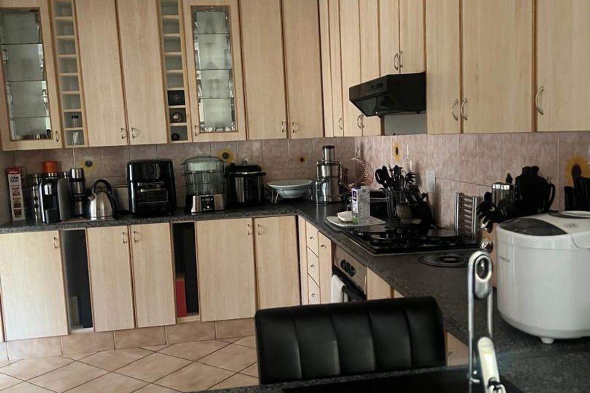 A functional kitchen featuring light wood-tone cabinetry, dark granite countertops, a gas hob with extractor fan, and tiled flooring.
