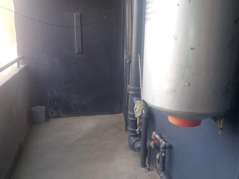 A utility area featuring an exposed electric water heater and plumbing infrastructure on a concrete balcony.
