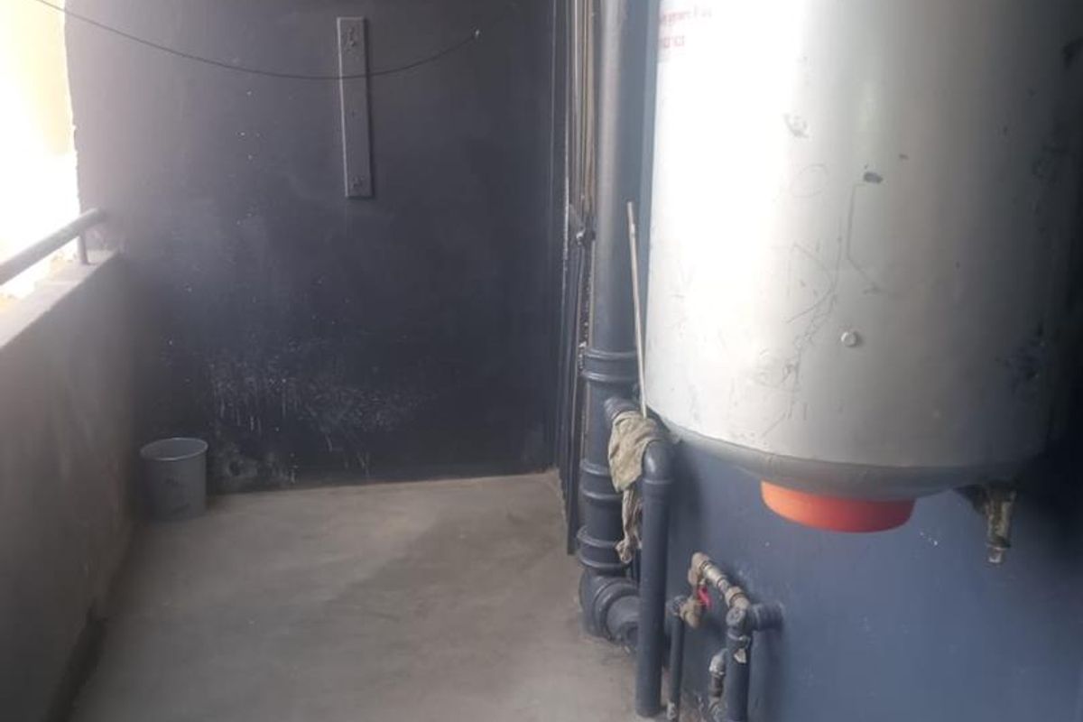 A utility area featuring an exposed electric water heater and plumbing infrastructure on a concrete balcony.