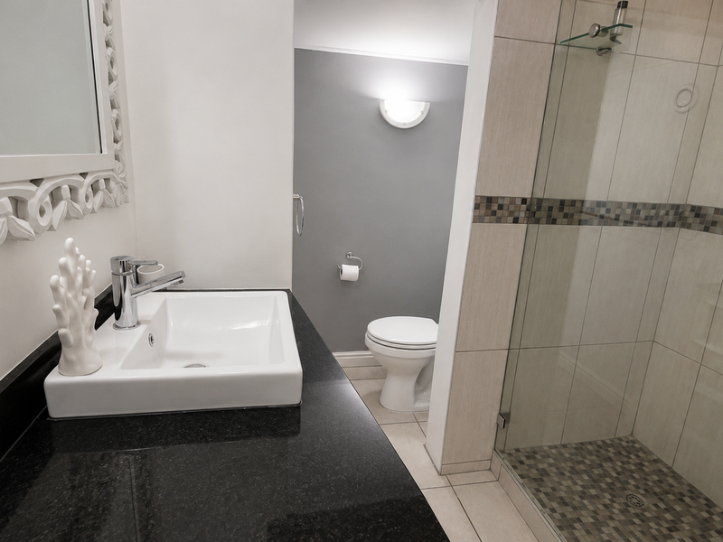 Modern bathroom featuring a granite vanity with a vessel sink, a glass-enclosed shower with mosaic tiling, and a wall-mounted toilet.
