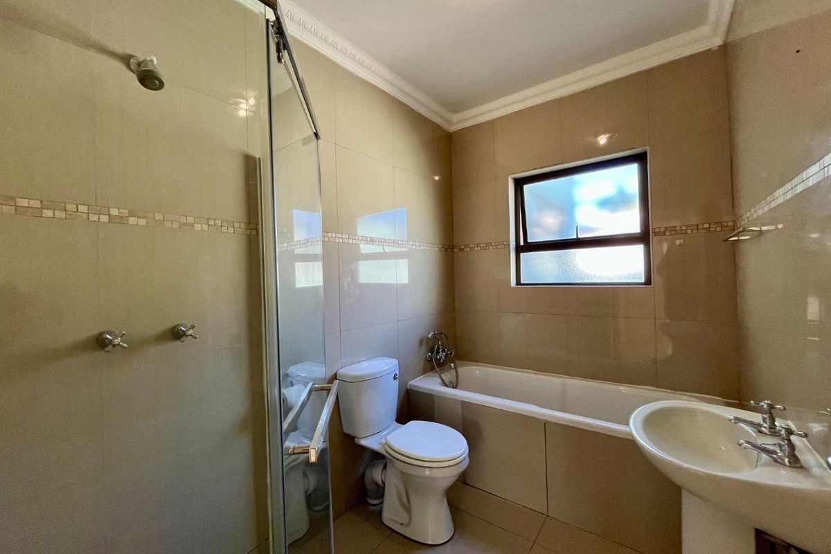 A functional bathroom featuring a glass-enclosed shower, a built-in bathtub, a pedestal sink, and neutral wall tiling with decorative accents.