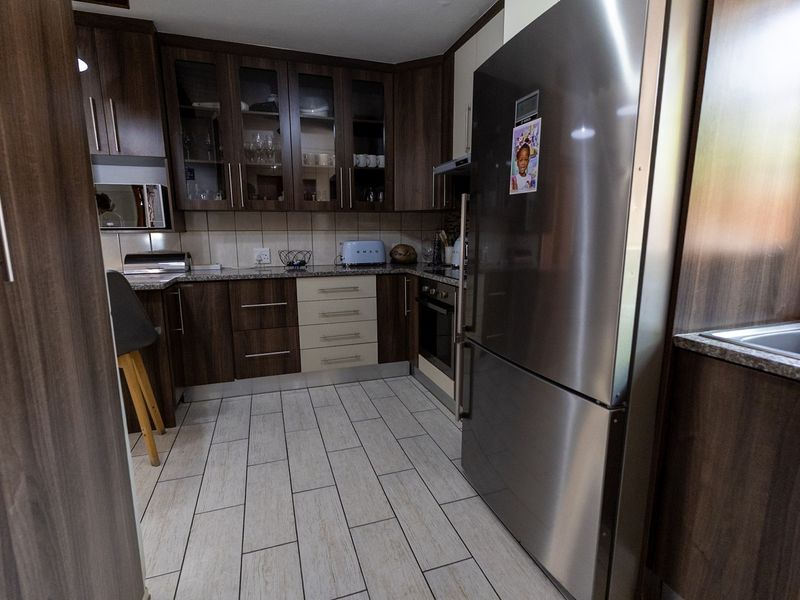 A modern kitchen featuring dark wood cabinetry, granite countertops, tiled flooring, and integrated appliances, offering a functional and well-maintained cooking space.